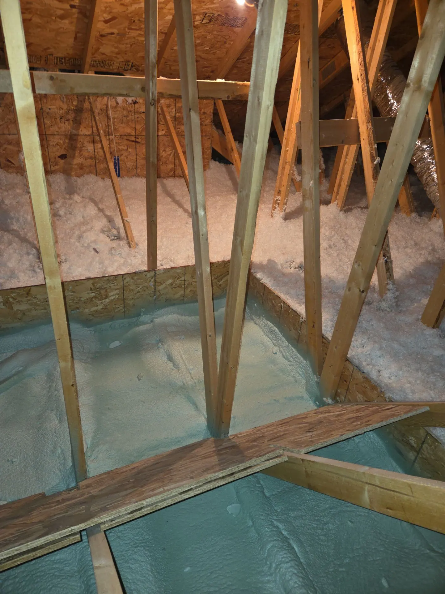 Spray foam applied across an attic floor between roof trusses